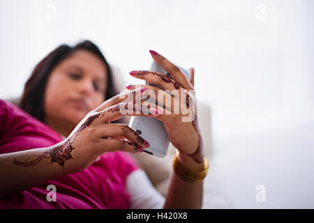 Femme avec des tatouages au henné sur les mains texting on cell phone Banque D'Images