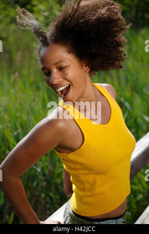 Jeune femme, rire, la peau sombre, pont, heureux, demi-portrait, les non-blancs, boucles, aux cheveux bruns, l'été, le soleil, profiter, loisirs, vacances, drôlement la vie, la joie, le plaisir, la joie, l'insouciance, de désinvolture, exhilarates, motion, top, débardeur, résumé, jaune, fondu, de la jeunesse, amuse, heureux, vivacité, vitalité, impulsivement, positivement, l'humeur, de transmission, de naturel, à l'extérieur de la jetée en bois, stand, mode de vie, Banque D'Images