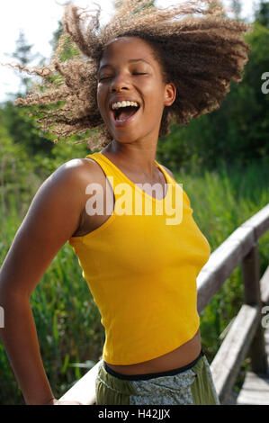 Jeune femme, rire, la peau sombre, pont, heureux, demi-portrait, les non-blancs, boucles, aux cheveux bruns, l'été, le soleil, profiter, loisirs, vacances, drôlement la vie, la joie, le plaisir, la joie, l'insouciance, de désinvolture, exhilarates, heureux, motion, top, débardeur, résumé, jaune, fondu, de la jeunesse, amuse, vivacité, vitalité, impulsivement, positivement, l'humeur, de transmission, de naturel, à l'extérieur de la jetée en bois, stand, mode de vie, Banque D'Images