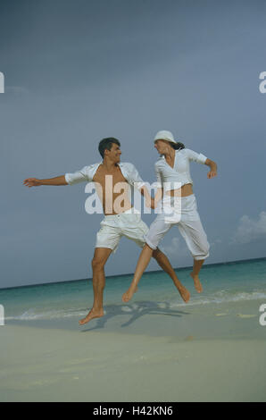 Jeune couple, jump, mer, prêt, heureux, modèle sorti, corps entier, personne, homme, femme, le contact oculaire, vacances, été, mode de vie, tombe dans l'amour, blanc, loisirs, activement, motion, bien formé, aux cheveux bruns, pieds nus, joliment, plage de sable, l'océan, vacances de rêve, ensemble, les uns avec les autres, de façon positive, sportily, à l'extérieur, coiffures, soins, vêtements de sport, caper, exubérance, Banque D'Images