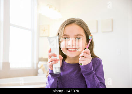 Smiling Caucasian girl holding toothbrush et tube de dentifrice dans la salle de bains Banque D'Images