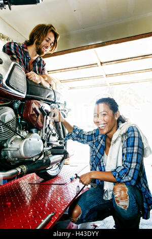 Man Watching laughing woman la réparation en garage moto Banque D'Images