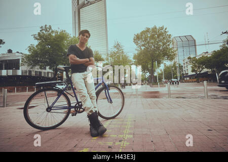 Smiling Young man leaning on bicycle in city Banque D'Images