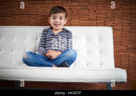 Boy assis en tailleur sur le canapé Banque D'Images