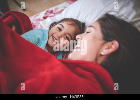 Laughing Caucasian mother and daughter sous couverture rouge au lit Banque D'Images