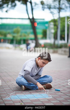 Boy encombrement coffre avec la craie sur trottoir Banque D'Images