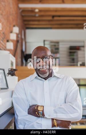 Smiling man with arms crossed leaning on manteau Banque D'Images