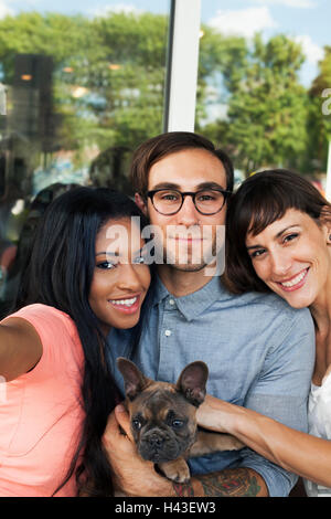 Les amis posant avec chien pour selfies Banque D'Images