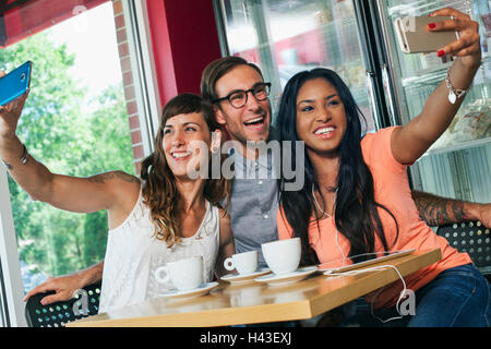 Les amis de prendre cell phone in coffee shop selfies Banque D'Images