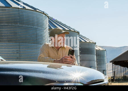 Caucasian farmer leaning on truck texting on cell phone Banque D'Images