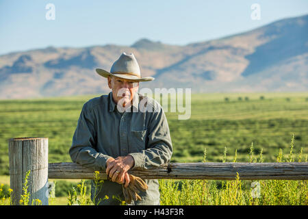 Caucasian farmer holding gloves leaning on wooden fence Banque D'Images