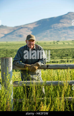 Caucasian farmer portant des gants leaning on wooden fence Banque D'Images