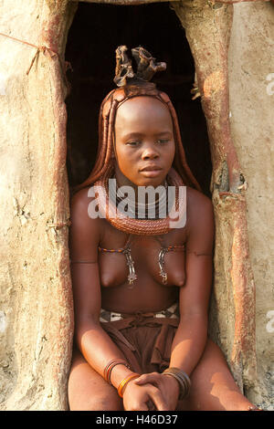 L'Afrique, la Namibie, la région Kunene, Kaokoveld, Himba, jeune fille assis, cabane, d'entrée, Banque D'Images