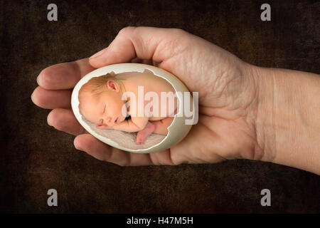 Bébé nouveau-né de dormir dans un oeuf cassé, tenue par une femme. Banque D'Images