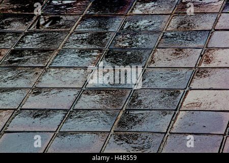 Close up of abstract grunge textures et motifs se brouille avec la lumière et l'obscurité des réflexions sur une chaussée mouillée fond carreaux Banque D'Images
