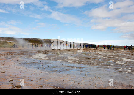 Les gens se tenant sur les armes chimiques et les dépôts géologiques causés par le débordement de l'eau du geyser geysir Islande Banque D'Images