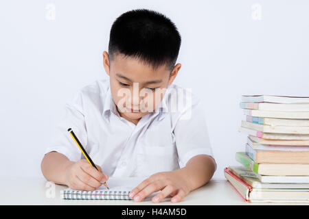 Chinois asiatique petit garçon portant l'uniforme des élèves de l'écriture en langage clair devoirs fond blanc isolé. Banque D'Images