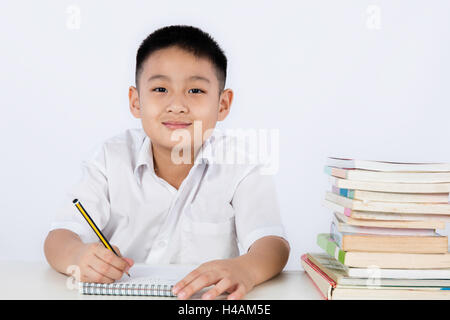 Chinois asiatique petit garçon portant l'uniforme des élèves de l'écriture en langage clair devoirs fond blanc isolé. Banque D'Images