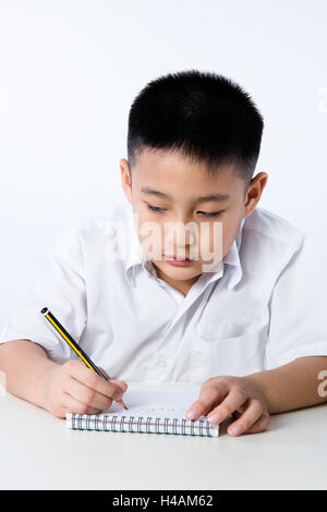 Chinois asiatique petit garçon portant l'uniforme des élèves de l'écriture en langage clair devoirs fond blanc isolé. Banque D'Images