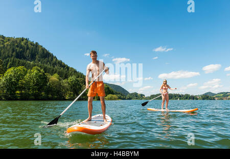 Jeune homme et femme sur paddle boards, à l'aide de stand-up paddles, lac Schliersee, Haute-Bavière, Bayern, Allemagne Banque D'Images