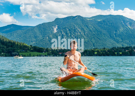 Jeune homme assis sur un paddle board sur le lac Schliersee, Upper Bavaria, Bavaria, Germany Banque D'Images
