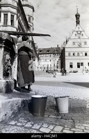 Zwei Frauen verwalten sich während Sie die Wassereimer mit Wasser aus dem Springbrunnen Am Marktplatz vor dem Rathaus und der Ratstrinkstube voll laufen lassen, Rothenburg ob der Tauber, Allemagne Allemagne Années 1930 er Jahre. Deux femmes ayant un chat tandis que le buckte Banque D'Images