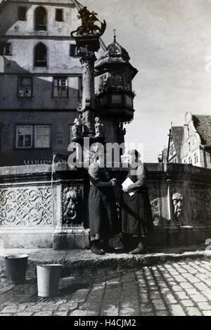 Zwei Frauen verwalten sich während Sie die Wassereimer mit Wasser aus dem Springbrunnen vor dem Rathaus imposanten voll laufen lassen, Rothenburg ob der Tauber, Allemagne Allemagne Années 1930 er Jahre. Deux femmes ayant un chat tandis que le bucktes sont remplissage avec de l'eau f Banque D'Images
