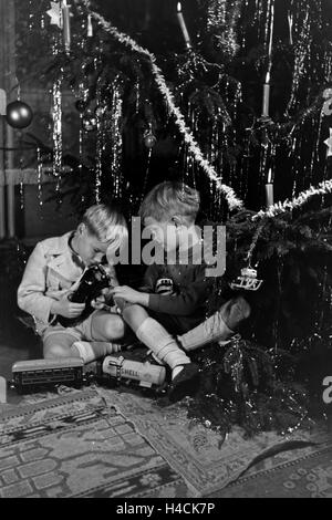 Zwei Jungen spielen am Weihnachtsabend Unter dem Tannenbaum mit der neuen Modelleisenbahn, Deutschland 1938. Deux garçons jouant avec le nouveau model train sous l'arbre de Noël, de l'Allemagne 1930 Banque D'Images