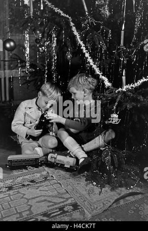 Zwei Jungen spielen am Weihnachtsabend Unter dem Tannenbaum mit der neuen Modelleisenbahn, Deutschland 1938. Deux garçons jouant avec le nouveau model train sous l'arbre de Noël, de l'Allemagne 1930 Banque D'Images