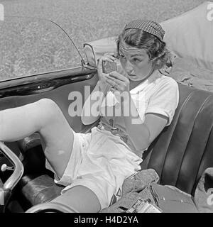 Eine junge Frau schminkt sich auf dem Rücksitz eines Cabrios, Deutschand er Jahre 1930. Une jeune femme faisant son faire jusqu'à la banquette arrière d'un cabriolet, Allemagne 1930. Banque D'Images