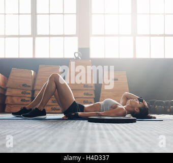 Jeune femme allongée sur le dos dans la salle de sport après son entraînement. Femme de remise en forme pour se détendre après votre séance d'exercice.