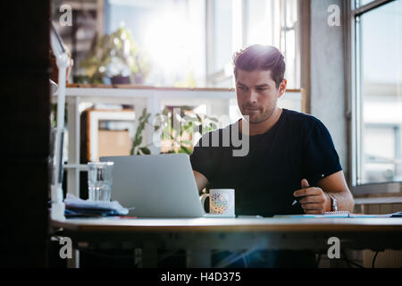 Photo de beau jeune homme assis à son bureau et de la rédaction de notes. Man dans son bureau. Banque D'Images