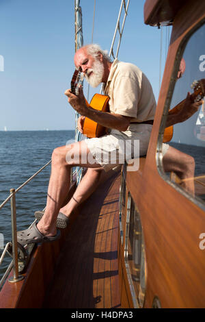 Homme plus âgé sur son bateau à voile joue de la guitare Banque D'Images