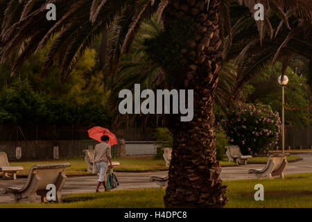 Femme avec un parapluie rouge balade dans le parc de la promenade à Laredo, Cantabrie, Espagne, Europe. Banque D'Images