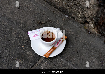 Partiellement fini espresso est laissé sur la chaussée en bord de mur en pierre. Deux paquets non ouverts du sucre sur la soucoupe. Banque D'Images