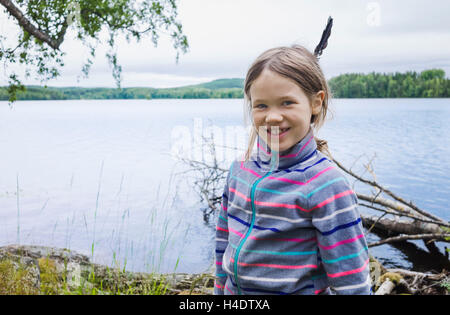 Fille avec d'une plume dans les cheveux se dresse sur la rive d'un lac et de sourires dans l'appareil photo Banque D'Images