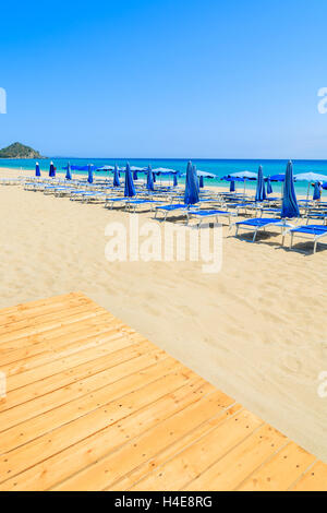 Passerelle en bois et de chaises longues avec parasols sur la plage de sable de Cala Sinzias, Sardaigne, île, Italie Banque D'Images