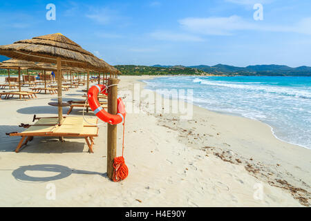 Chaises longues avec parasols et bouée rouge sur la plage de sable blanc dans la baie de Porto Giunco, Sardaigne, île, Italie Banque D'Images