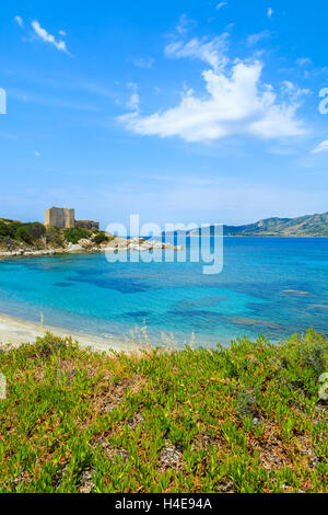 Plage avec la mer d'azur et château en arrière-plan, près de Porto Giunco, port de l'île de la Sardaigne, Italie Banque D'Images