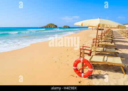 Chaises longues avec parasols et rouge bague la vie sur la plage de Chia, Sardaigne, île, Italie Banque D'Images