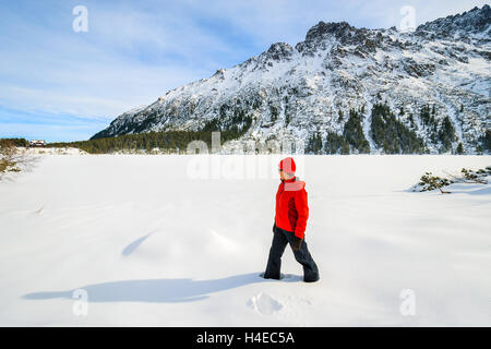 Jeune femme veste rouge en tourisme debout dans la neige profonde sur le lac Morskie Oko gelé en hiver, les montagnes Tatras, Pologne Banque D'Images