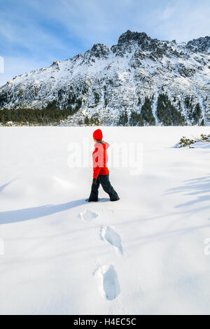 Jeune femme veste rouge en tourisme debout dans la neige profonde sur le lac Morskie Oko gelé en hiver, les montagnes Tatras, Pologne Banque D'Images