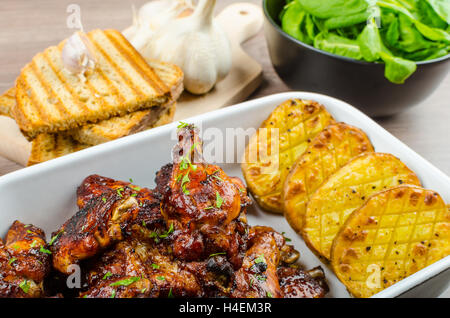 Les ailes de poulet avec du pain à l'ail panini, pommes de terre épicées rustique, feuilles d'épinards fraîches Banque D'Images