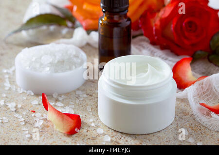 La crème pour le visage avec des roses, bouteille de aromathérapie huiles essentielles et de sel sur fond noir en marron. Rose Spa. Banque D'Images