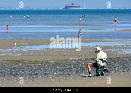 Homme plus âgé assis sur Ryde, Isle of Wight uk maison de plage à marée basse à dessiner une vue sur le Solent chaude journée d'été fort loins paddling Banque D'Images