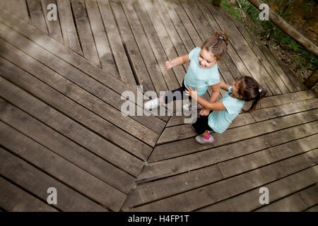 Grand angle de deux soeurs en souriant tee-shirt bleu de jouer et d'exécution sur wooden path in park Banque D'Images