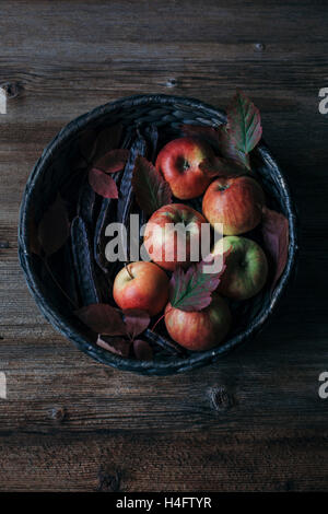 Pommes rouges organiques et de gousses de caroube dans un panier avec les feuilles d'automne Banque D'Images