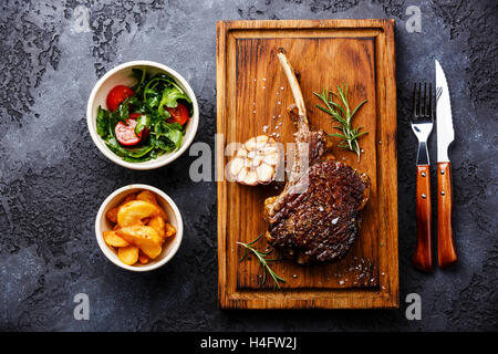 Barbecue grillé bifteck sur le ris de veau de l'os avec les quartiers de pommes de terre et salade de tomates et roquette sur fond sombre Banque D'Images