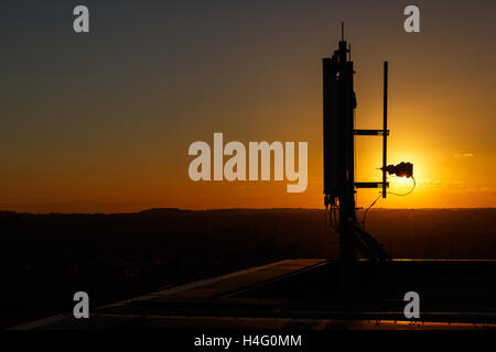 Mât / antenne de communications mobiles au sommet d'un grand bâtiment, contre le coucher du soleil. À Nottingham, Angleterre Banque D'Images