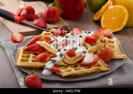 Gaufres maison au sirop d'érable et fraises, garni de crème et de chocolat, la boisson fraîche orange Banque D'Images